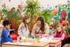Three children drawing with an adult surrounded by paintings and plants in DCA Gallery