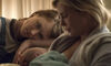 A woman looks on as another woman breastfeeds a baby