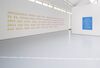 From Eve Fowler's exhibition. Yellow and pink text on a white wall says 'Patriarchal poetry deny why. Patriarchal poetry come by the way to go. Patriarchal poetry indirected. Patriarchal poetry at best. Best and most. Long and short. Left and right. There and more. Near and far. Gone and gone. Light and fair. Here and there. This and now. Felt and how. Next and near. In and on.'