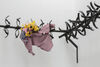 Black barbed metal work is seen in the corner of the gallery. A shirt and a bunch of flowers is shown snagged on the metal barbs. 
