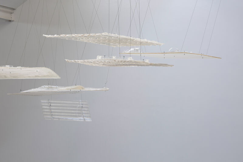 A series of hanging objects, white in colour, including metal sheets. 