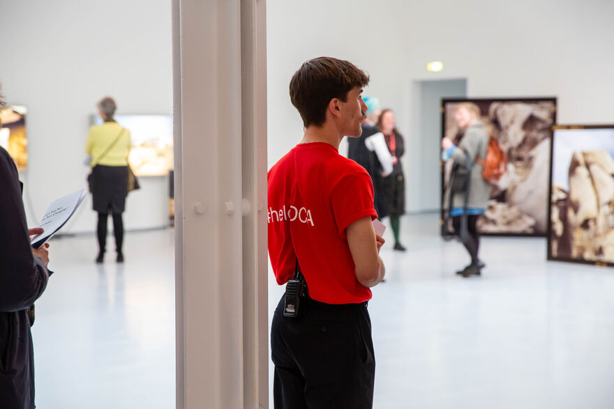A person in a red DCA t-shirt stands in Zineb Sedira's exhibition.
