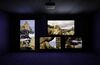 Four large screens in a darkened room showing images of rock formations in the sea.