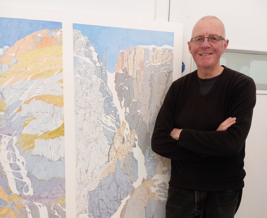 Man stands smiling beside a worl of art
