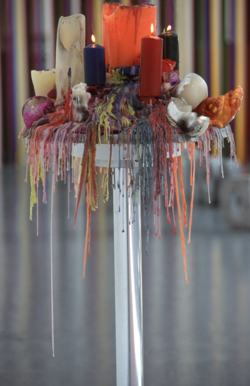 A high silver table is covered in colourful candles, which are melting everywhere.