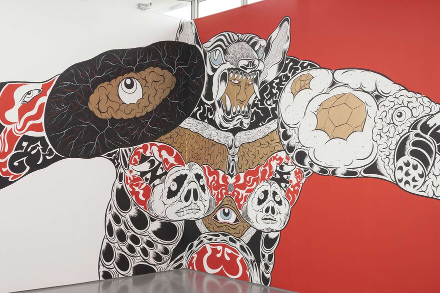 A large mural in beige, white, black and red as part of Hideyuki Katsumata's exhibition. The mural is of a man, who is massive and is wearing a strange costume made up of eyes and faces.